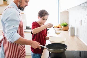 A mature father with small son indoors in kitchen, making pancakes. - HPIF19415