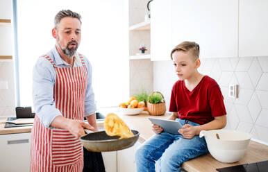 Ein reifer Vater mit seinem kleinen Sohn in der Küche, der Pfannkuchen macht. - HPIF19421