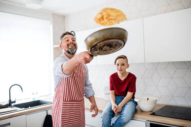 Ein reifer Vater mit seinem kleinen Sohn in der Küche, der Pfannkuchen wendet. - HPIF19422