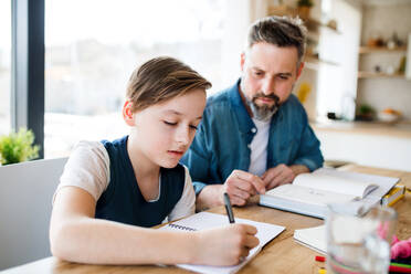 Ein reifer Vater mit seinem kleinen Sohn sitzt am Tisch in einem Haus und macht Hausaufgaben. - HPIF19437