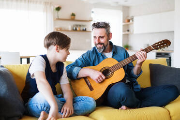 Ein reifer Vater mit seinem kleinen Sohn sitzt auf dem Sofa in einem Haus und spielt Gitarre. - HPIF19451