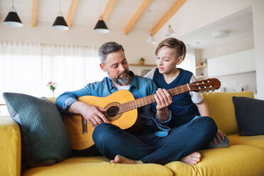 A mature father with small son sitting on sofa indoors, playing guitar.. - HPIF19452