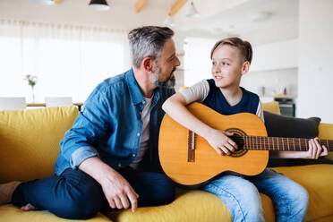 A mature father with small son sitting on sofa indoors, playing guitar. - HPIF19453