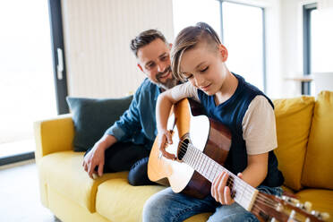 A mature father with small son sitting on sofa indoors, playing guitar. - HPIF19454
