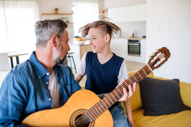 A mature father with small son sitting on sofa indoors, playing guitar. - HPIF19455