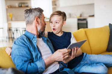 Ein reifer Vater mit seinem kleinen Sohn sitzt auf dem Sofa in einem Haus und benutzt ein Tablet. - HPIF19459