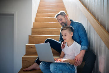 Ein reifer Vater mit kleinem Sohn sitzt auf der Treppe in einem Haus und benutzt einen Laptop. - HPIF19472