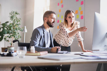 Zwei Geschäftsleute mit Rollstuhl im Büro arbeiten zusammen. - HPIF19502