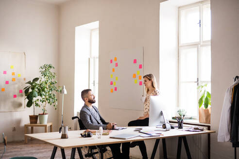 Zwei Geschäftsleute mit Rollstuhl im Büro arbeiten zusammen. - HPIF19503