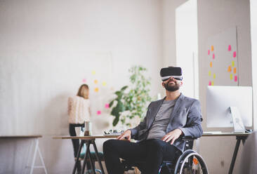 Zwei Geschäftsleute mit Rollstuhl im Büro arbeiten zusammen. Ein Mann trägt eine VR-Brille. - HPIF19504