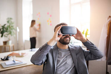 Two business people with wheelchair in the office working together. A man wearing VR goggles. - HPIF19506