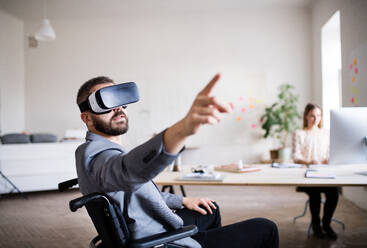 Zwei Geschäftsleute mit Rollstuhl im Büro arbeiten zusammen. Ein Mann trägt eine VR-Brille. - HPIF19511