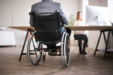 Zwei unerkennbare Geschäftsleute mit Rollstuhl im Büro arbeiten zusammen. - HPIF19512