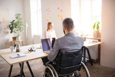 Zwei Geschäftsleute mit Rollstuhl im Büro arbeiten zusammen. - HPIF19513