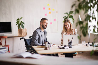 Two business people with wheelchair in the office working together. - HPIF19528