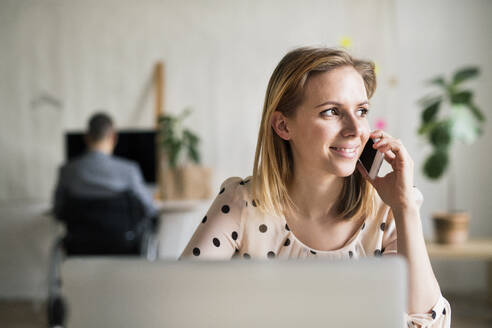 Zwei Geschäftsleute mit Rollstuhl und Smartphone arbeiten im Büro. - HPIF19533