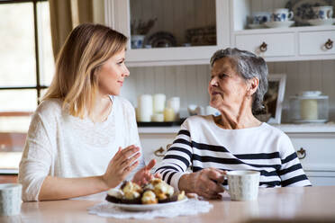 Portrait of an elderly grandmother with an adult granddaughter at home. Women sitting at the table, eating cakes and drinking coffee. - HPIF19608