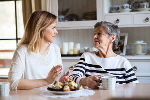 Porträt einer älteren Großmutter mit einer erwachsenen Enkelin zu Hause. Die Frauen sitzen am Tisch, essen Kuchen und trinken Kaffee. - HPIF19608