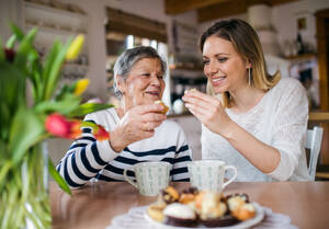 Porträt einer älteren Großmutter mit einer erwachsenen Enkelin zu Hause. Die Frauen sitzen am Tisch, essen Kuchen und trinken Kaffee. - HPIF19610