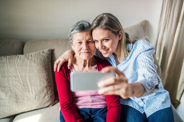 Generationsübergreifende Beziehungen durch Technologie: Oma und Enkelin halten Erinnerungen mit einem Selfie auf der Couch fest - HPIF19615