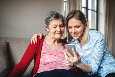 An elderly grandmother and adult granddaughter with smartphone at home. - HPIF19618