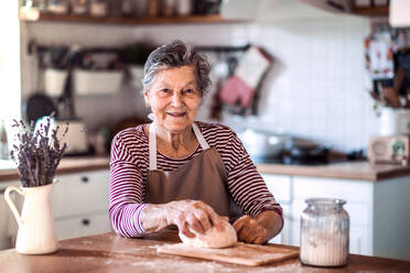 Das Porträt einer glücklichen älteren Frau, die zu Hause in der Küche Teig knetet. - HPIF19644