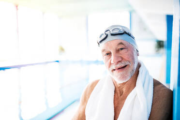 Älterer Mann, der mit einem Handtuch um den Hals an einem Hallenbad steht. Aktiver Rentner beim Sport. - HPIF19649