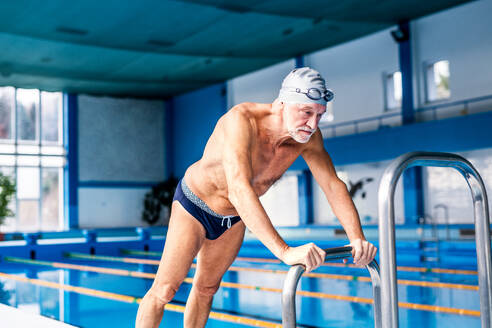 Älterer Mann steht am Hallenbad und dehnt sich. Aktiver Rentner beim Sport. - HPIF19654