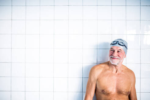 Porträt eines älteren Mannes vor weißem Hintergrund in einem Hallenbad. Aktiver Rentner beim Sport. - HPIF19659