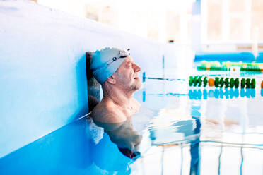 Älterer Mann schwimmt stehend im Wasser in einem Hallenbad. Aktiver Rentner beim Sport. - HPIF19664