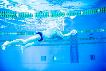 Senior man swimming underwater in an indoor swimming pool. Active pensioner enjoying sport. - HPIF19673