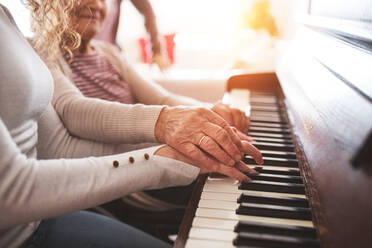 An unrecognizable teenage girl with grandmother playing the piano at home. Family and generations concept. - HPIF19694