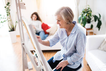 A mother or a grandmother with a teenage girl at home, painting. Family and generations concept. - HPIF19697