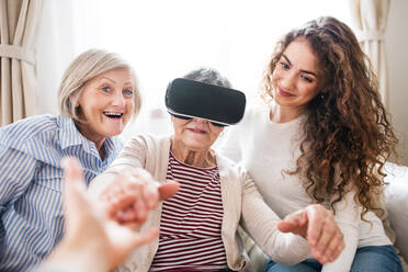 Ein Mädchen im Teenageralter, ihre Mutter und ihre Großmutter mit einer VR-Brille zu Hause: Familien- und Generationenkonzept. - HPIF19703