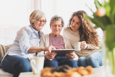 Ein Mädchen im Teenageralter, ihre Mutter und ihre Großmutter mit einem Tablet zu Hause - das Konzept der Familie und der Generationen. - HPIF19719