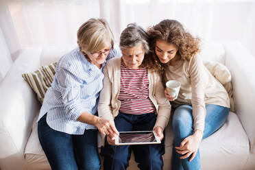 A teenage girl, her mother and grandmother with tablet at home. Family and generations concept. - HPIF19721