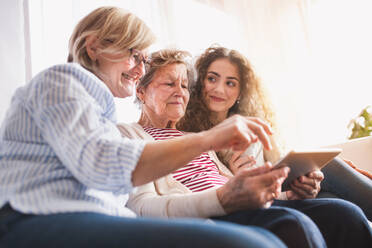 Ein Mädchen im Teenageralter, ihre Mutter und ihre Großmutter mit einem Tablet zu Hause - das Konzept der Familie und der Generationen. - HPIF19722