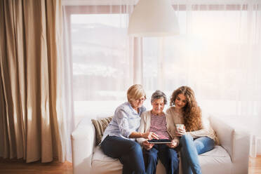 A teenage girl, her mother and grandmother with tablet at home. Family and generations concept. - HPIF19723