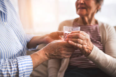 Two unrecognizable senior women at home, holding a glass of water. Family and generations concept. - HPIF19728