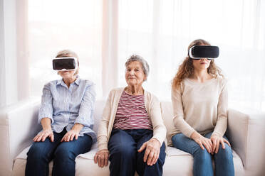 Ein Mädchen im Teenageralter, ihre Mutter und ihre Großmutter mit einer VR-Brille zu Hause: Familien- und Generationenkonzept. - HPIF19735