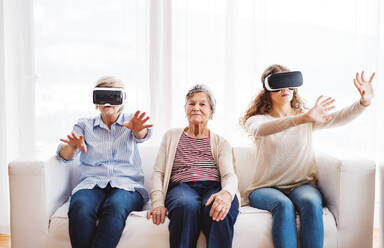 A teenage girl, her mother and grandmother with VR goggles at home. Family and generations concept. - HPIF19736