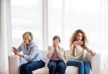 A teenage girl, her mother and grandmother with smartphone at home. Family and generations concept. - HPIF19738