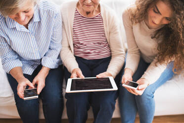 A teenage girl, her mother and unrecognizable grandmother with tablet and smartphones at home. Family and generations concept. - HPIF19740