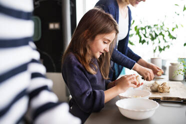 Ein kleines Mädchen mit einer nicht wiederzuerkennenden Mutter und Großmutter, die zu Hause kochen - ein Konzept für Familie und Generationen. - HPIF19771