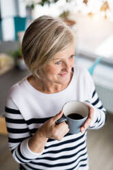 Ältere Frau in der Küche. Eine alte Frau im Haus, die eine Tasse Kaffee in der Hand hält. - HPIF19791