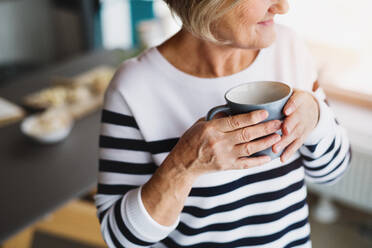 Eine unerkennbare ältere Frau in der Küche. Eine alte Frau im Haus, die eine Tasse Kaffee in der Hand hält. - HPIF19793