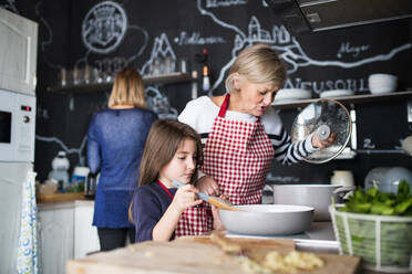 Ein kleines Mädchen mit ihrer Mutter und Großmutter zu Hause, beim Kochen. Familien- und Generationenkonzept. - HPIF19797