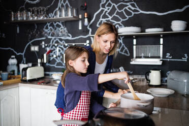 Ein kleines Mädchen, das mit seiner Mutter zu Hause kocht - ein Konzept für Familie und Generationen. - HPIF19807