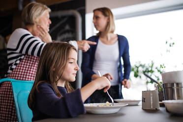 Ein kleines Mädchen mit ihrer Mutter und ihrer Großmutter zu Hause beim Essen - das Konzept der Familie und der Generationen. - HPIF19810