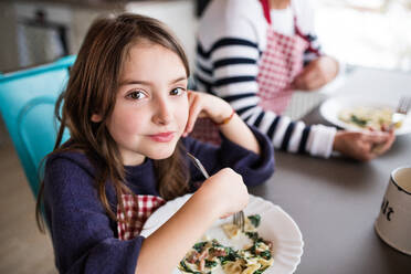 A small girl with unrecognizable grandmother at home, eating. Family and generations concept. - HPIF19811